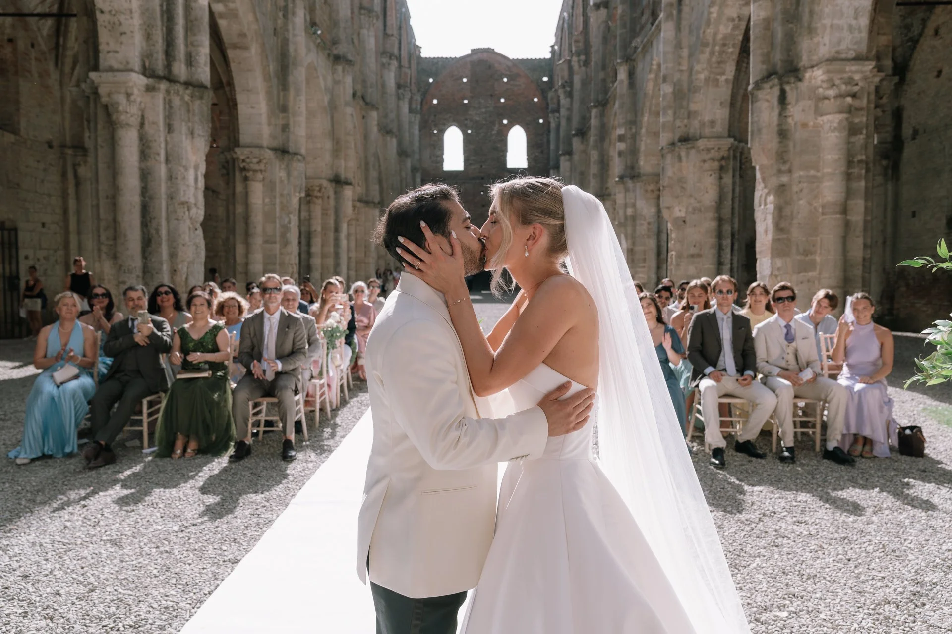 Bride and groom share their first kiss immediately after exchanging wedding rings during the ceremony at San Galgano, Chiusdino, Siena, Tuscany.