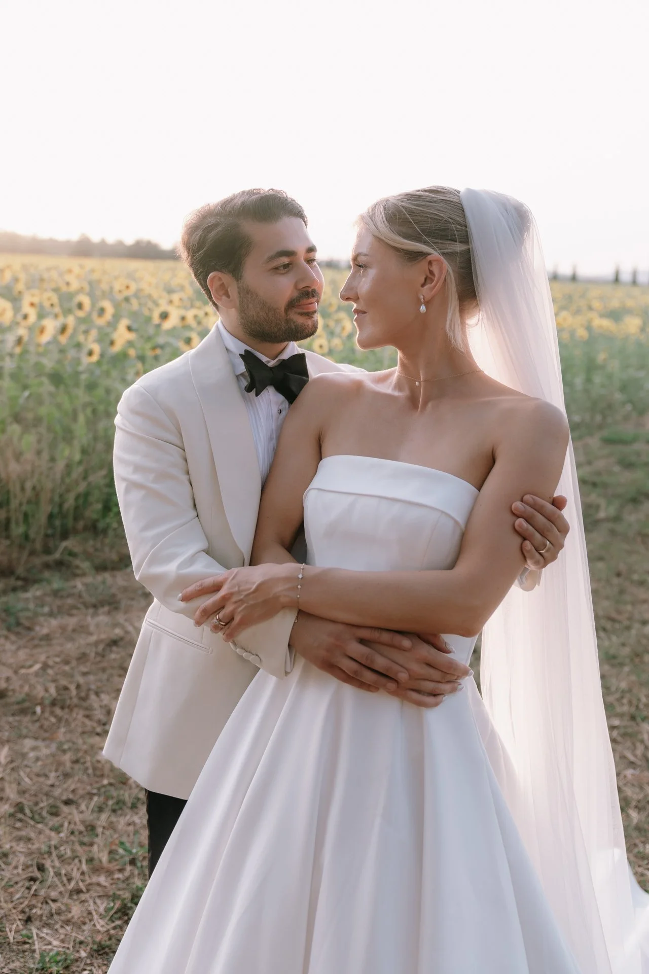 Bride and groom embracing in a blooming sunflower field at golden hour near San Galgano Tuscany