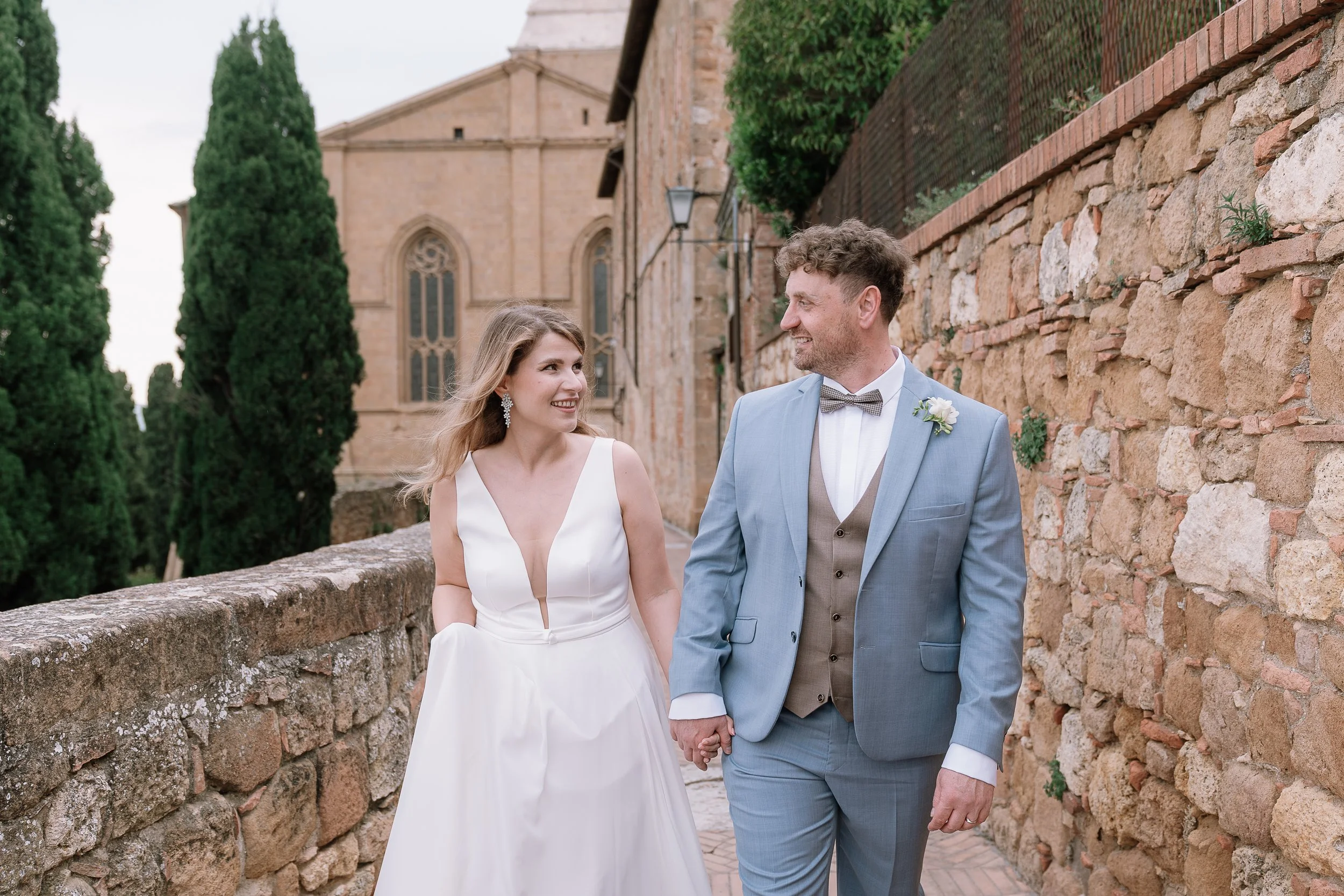 Bride and groom walking hand in hand through the romantic historic streets of Pienza Tuscany.