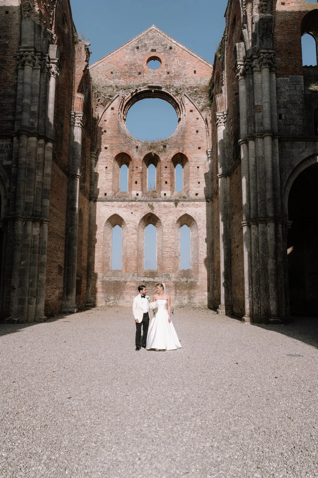 Bride and groom portrait walking down the open-air aisle of Abbey of San Galgano in Siena