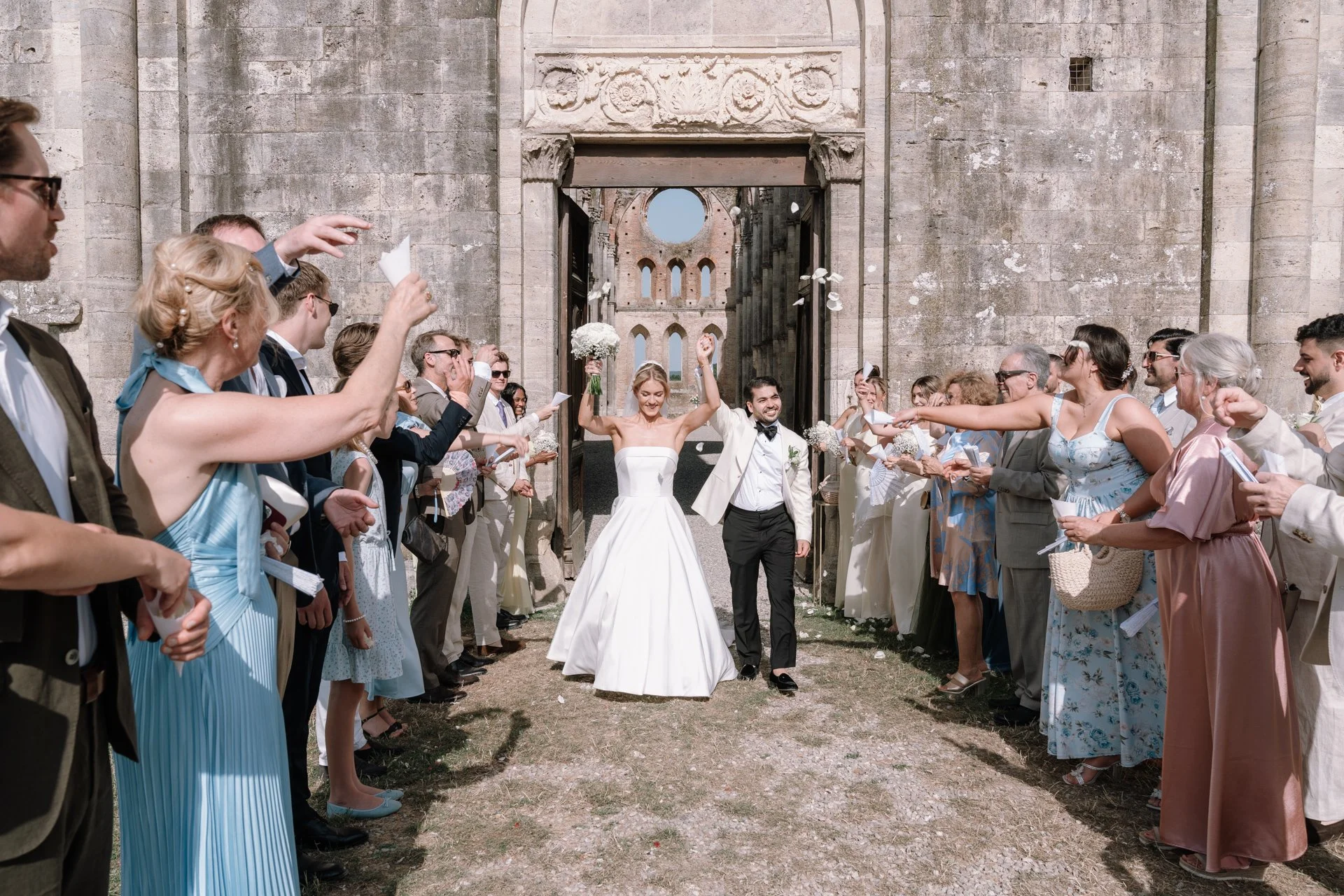 Newlyweds celebrated by guests while walking out of the aisle at San Galgano Abbey wedding.
