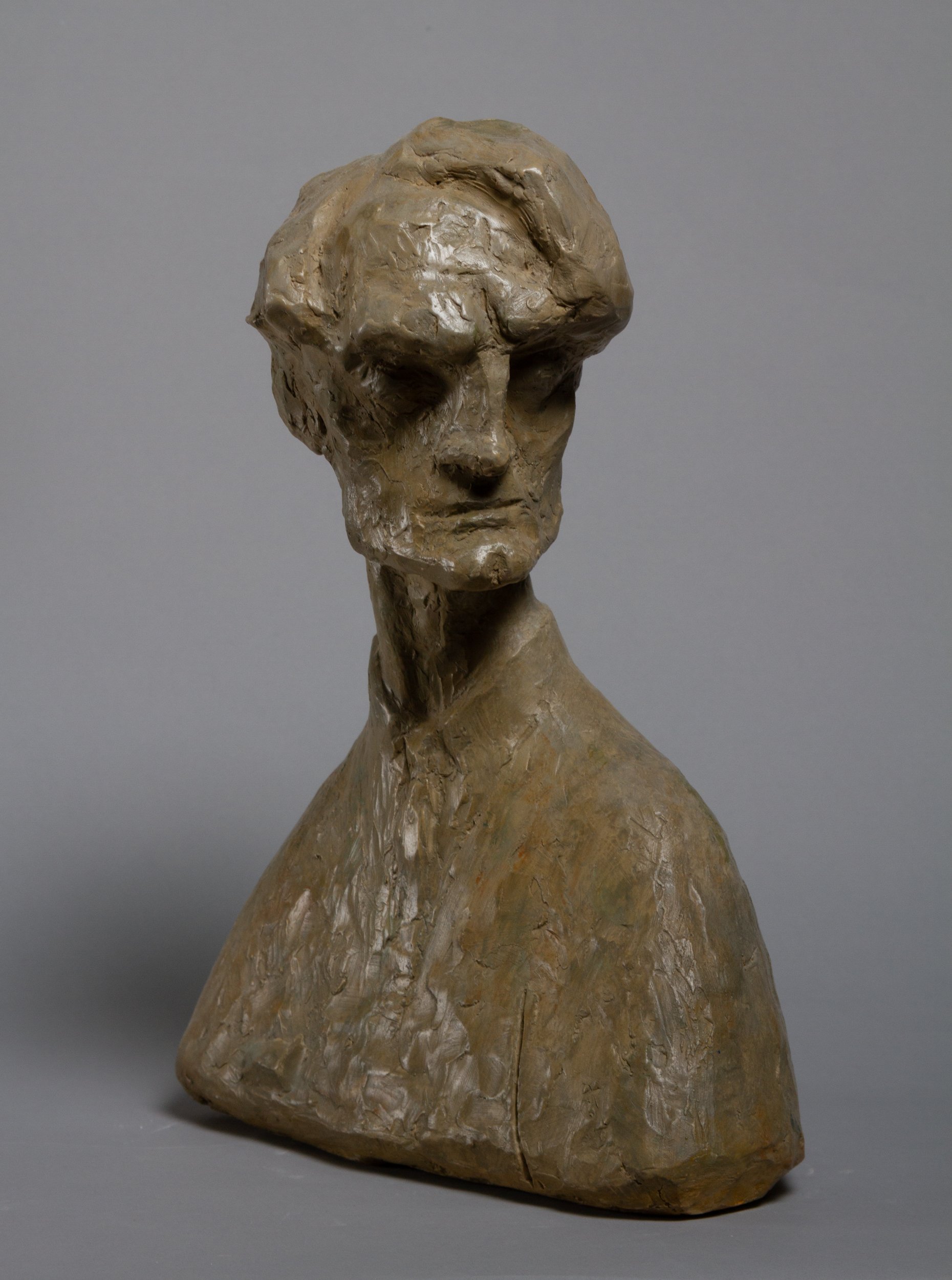 A sculpture of a human head and upper torso made of clay, with a rough, textured surface and a neutral expression.