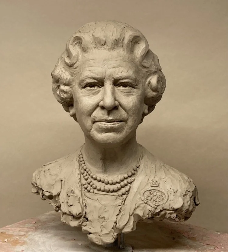 Clay bust sculpture of a woman with short, curly hair, wearing a necklace and a patterned top.