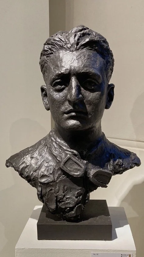 A bronze bust sculpture of a woman in military uniform with goggles, on a black stand.