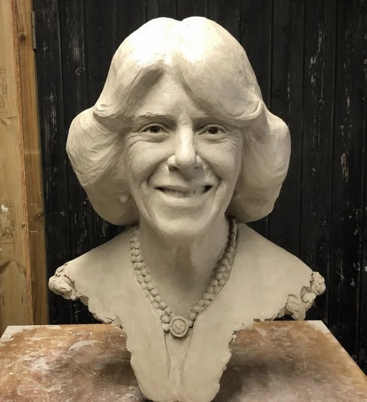 A clay bust sculpture of a woman with a smiling face, wavy hair, and a beaded necklace.