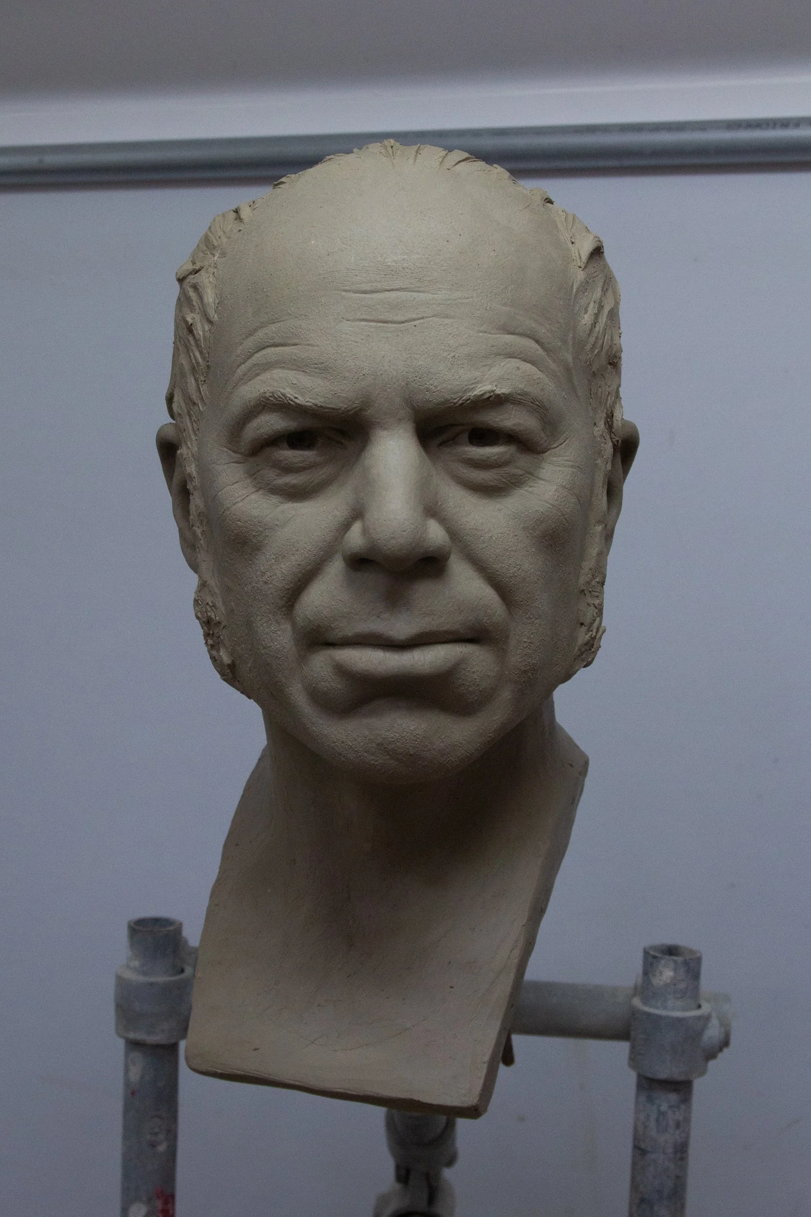 Sculpture of an older man's head on a stand, with detailed facial features and textured hair, set against a plain background.
