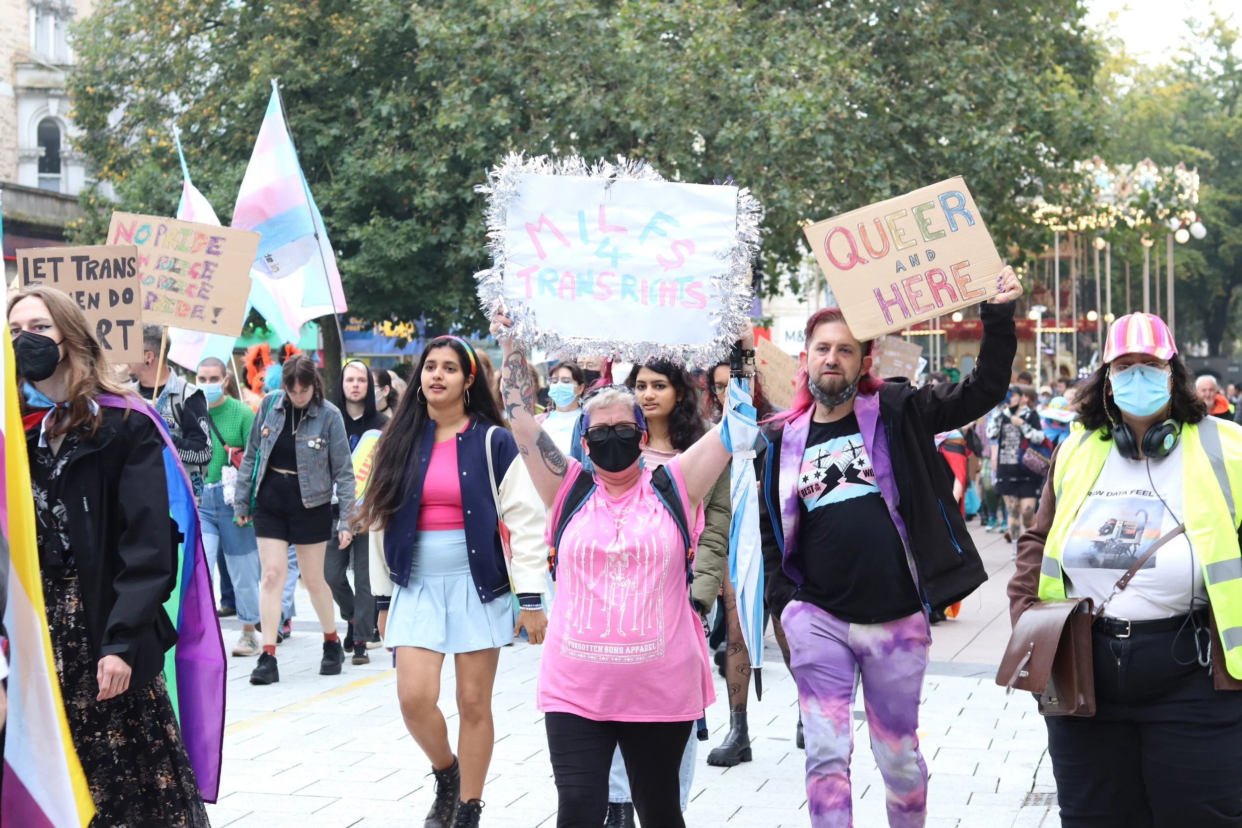 Group of people participating in a Pride parade, holding various signs and flags celebrating LGBTQ+ rights and diversity.