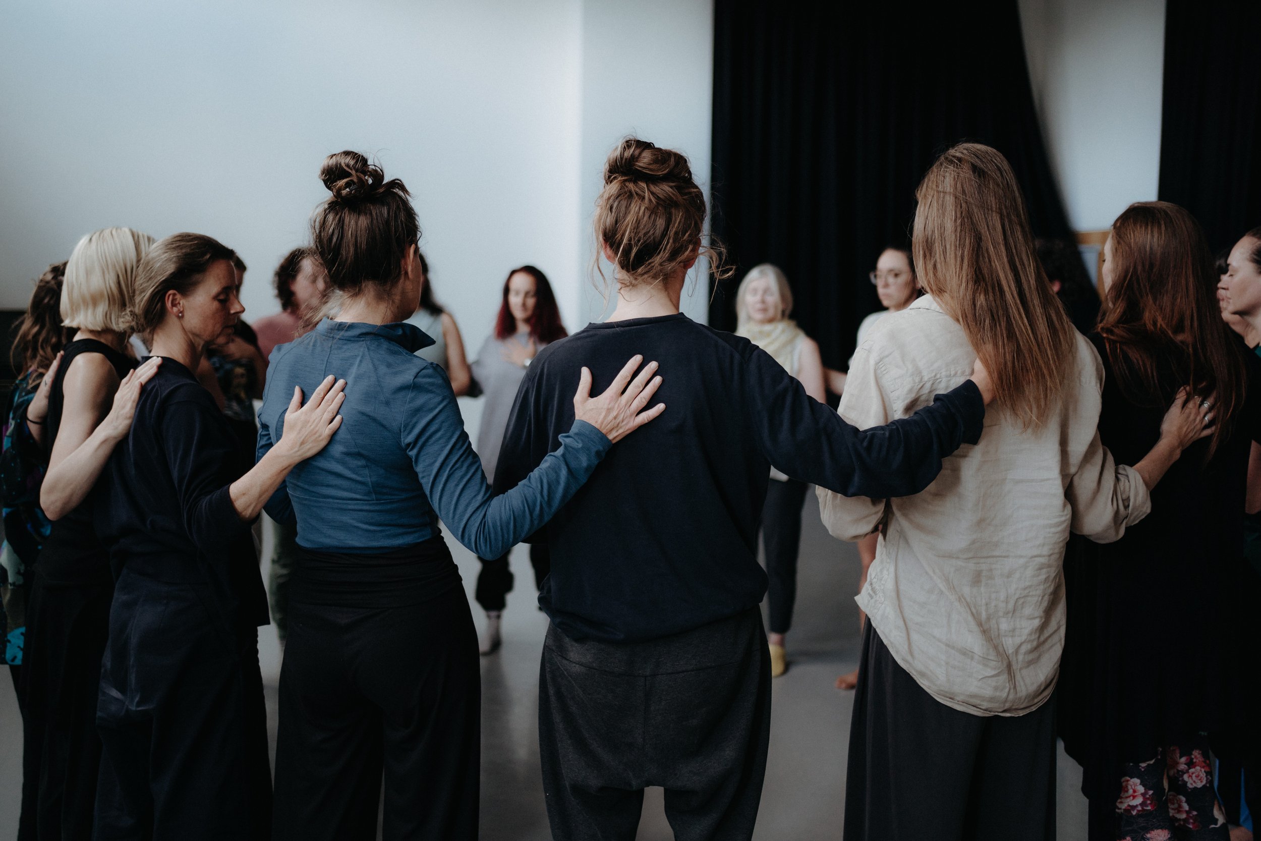 A group of women standing in a circle, placing hands on each other's shoulders in a supportive and comforting manner.