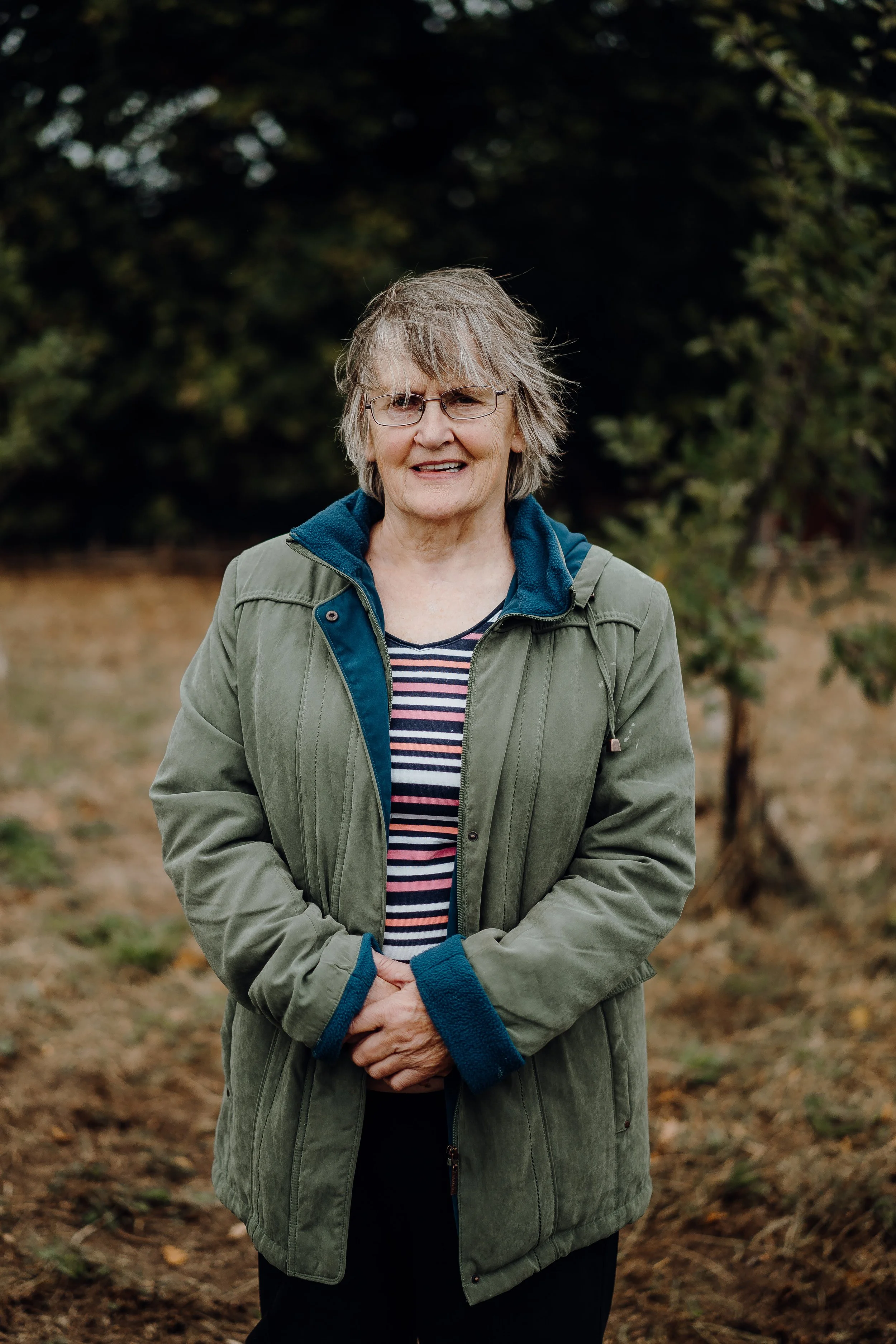 A woman wearing glasses and a green jacket standing outdoors.