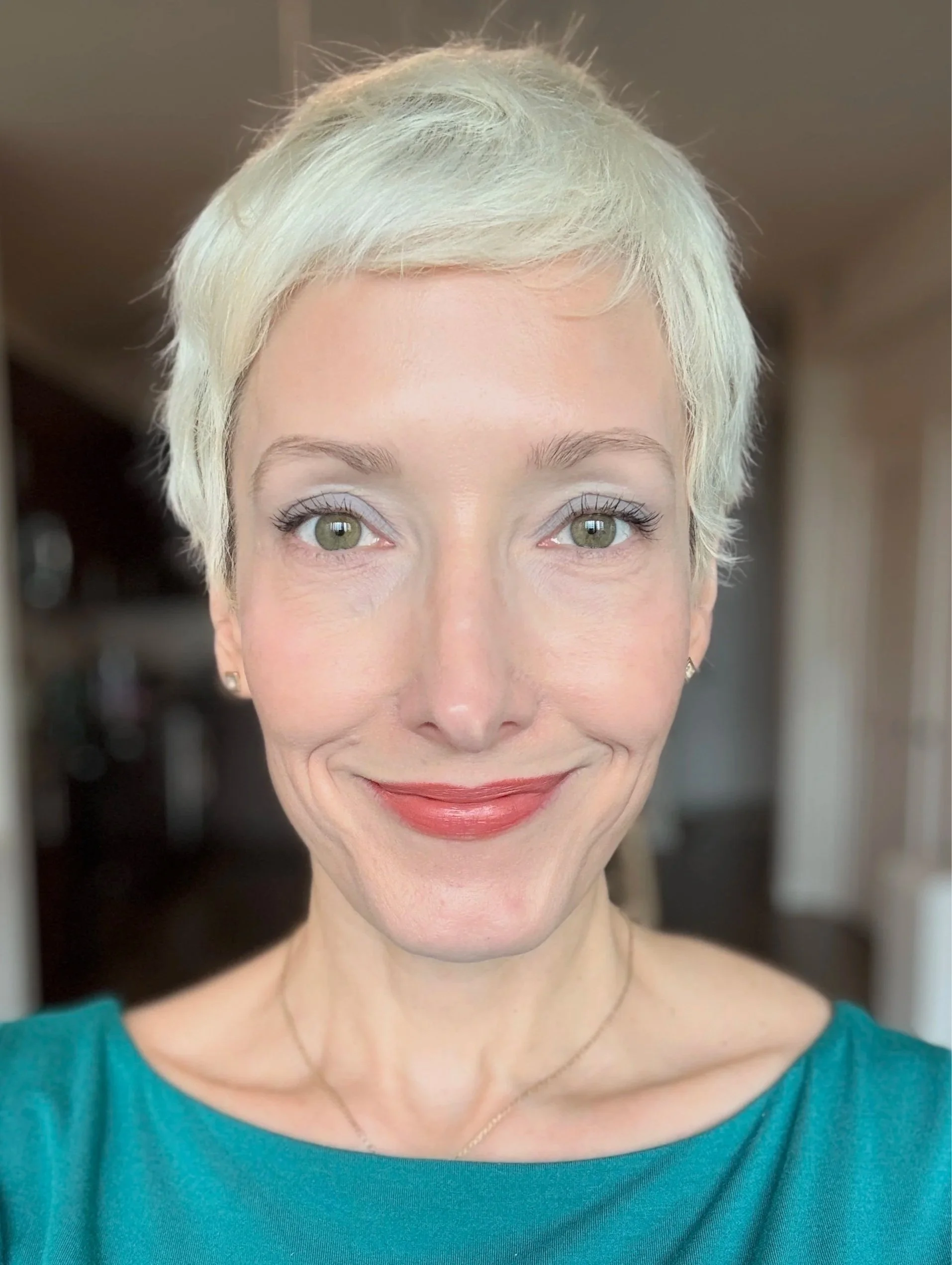 Close-up of a woman with short white hair, light makeup, and wearing a teal top.