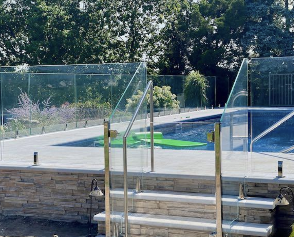 Frameless glass pool fence installed around a modern backyard pool with stone retaining wall in a Toronto landscape design.