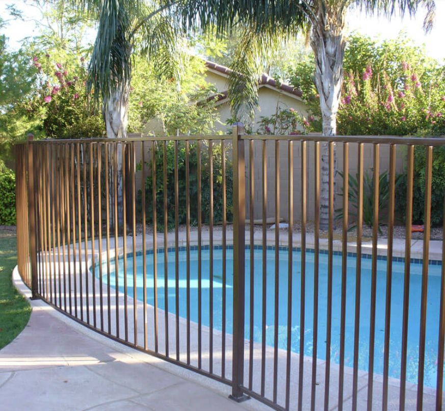 Vertical metal pool fencing enclosing a backyard swimming pool with tropical-style planting and modern landscape design.