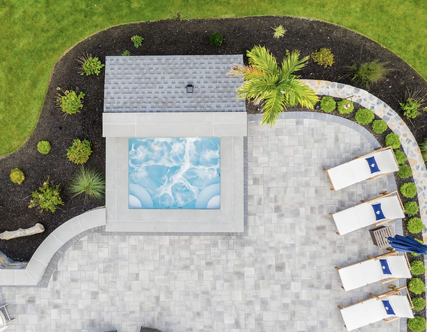 Aerial view of a modern backyard pool with light stone pavers, curved patio layout, and minimalist landscape design.