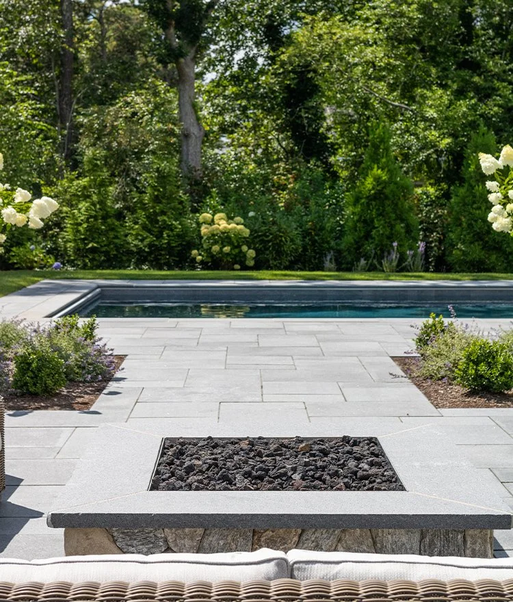 Modern poolside patio with large stone pavers and minimalist fire feature in landscaped backyard