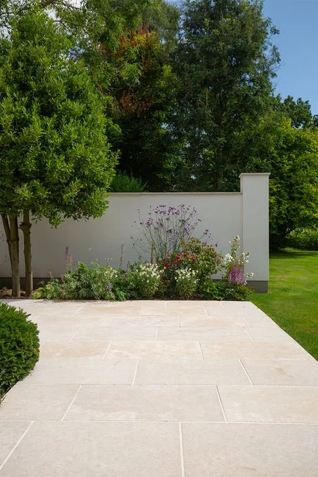 Minimalist stone patio surrounded by lawn and garden planting in a residential backyard