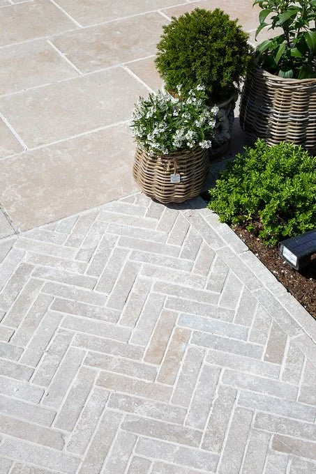 Light-coloured stone pavers laid in a herringbone pattern beside garden planters