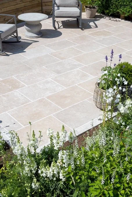 Natural stone patio with soft-toned pavers bordered by flowering garden plants