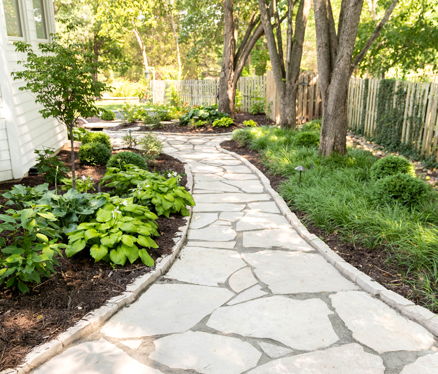 Curved flagstone walkway winding through lush garden planting and mature trees