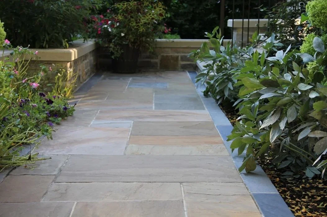 Stone patio walkway framed by raised planters and layered garden greenery