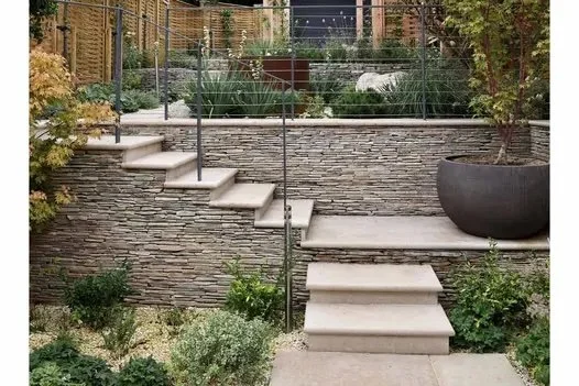 Stone garden steps with retaining wall and metal railing in a landscaped yard