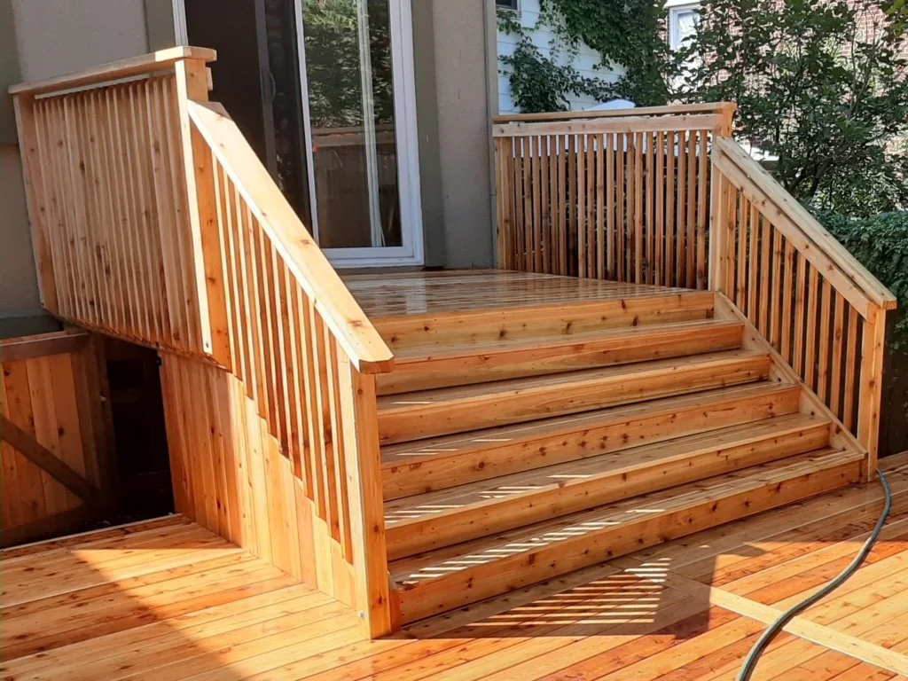 Pressure-treated wood deck stairs with matching railings leading to backyard patio entrance.