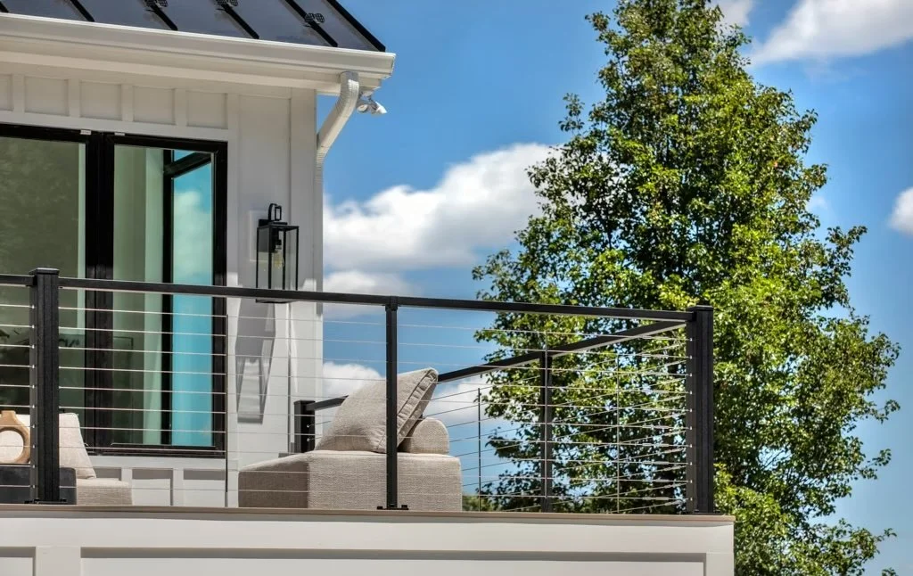 Contemporary raised deck with black metal and cable railing, white exterior home, and outdoor seating area.