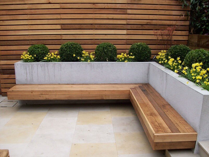 Modern backyard seating area with built-in wood bench, concrete planter wall, and horizontal privacy fence.