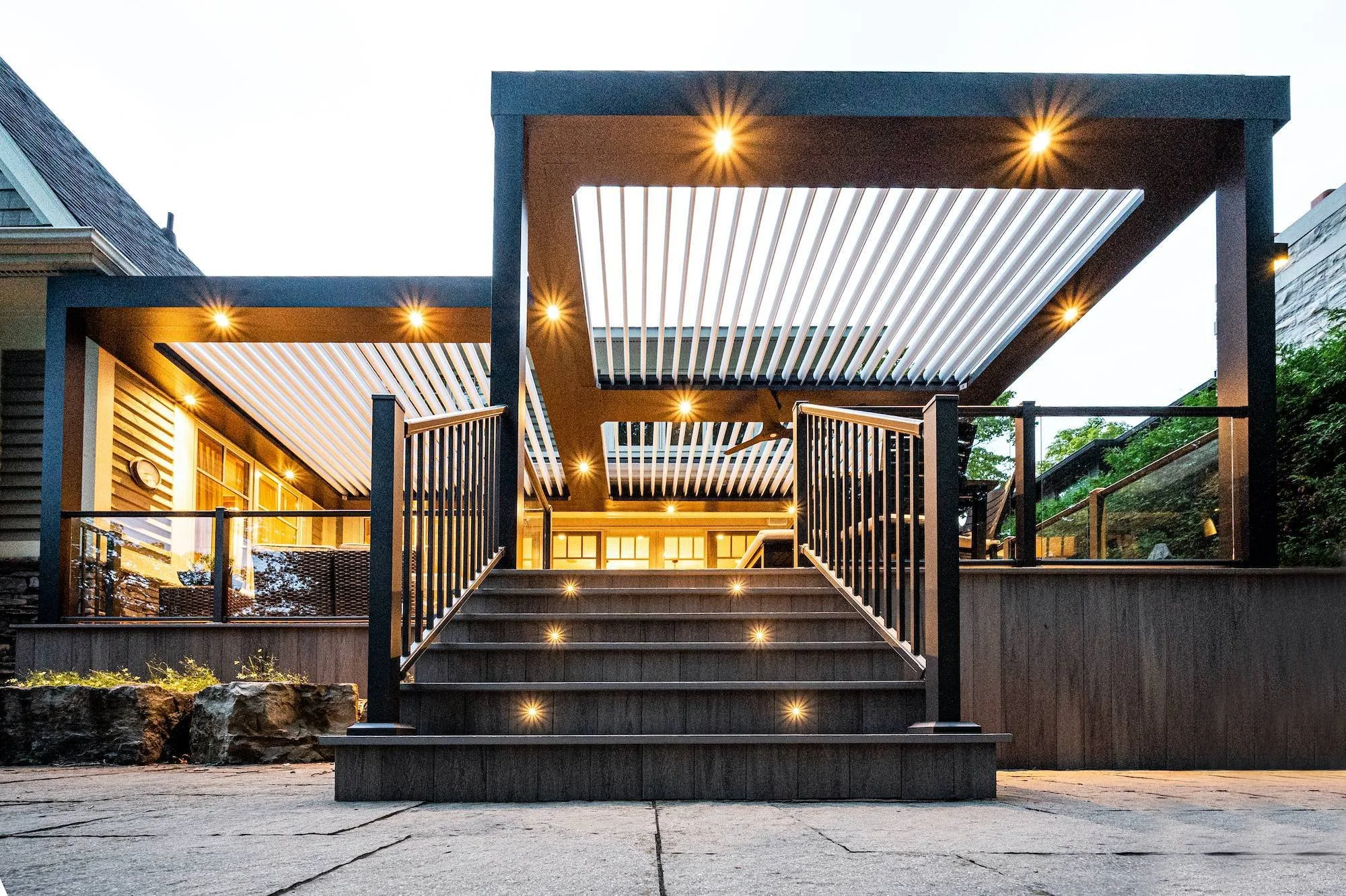 Covered backyard deck with pergola, integrated ceiling lights, and illuminated stairs for evening entertaining.