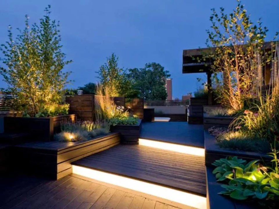 Contemporary tiered deck with soft LED strip lighting and landscaped garden beds at dusk.