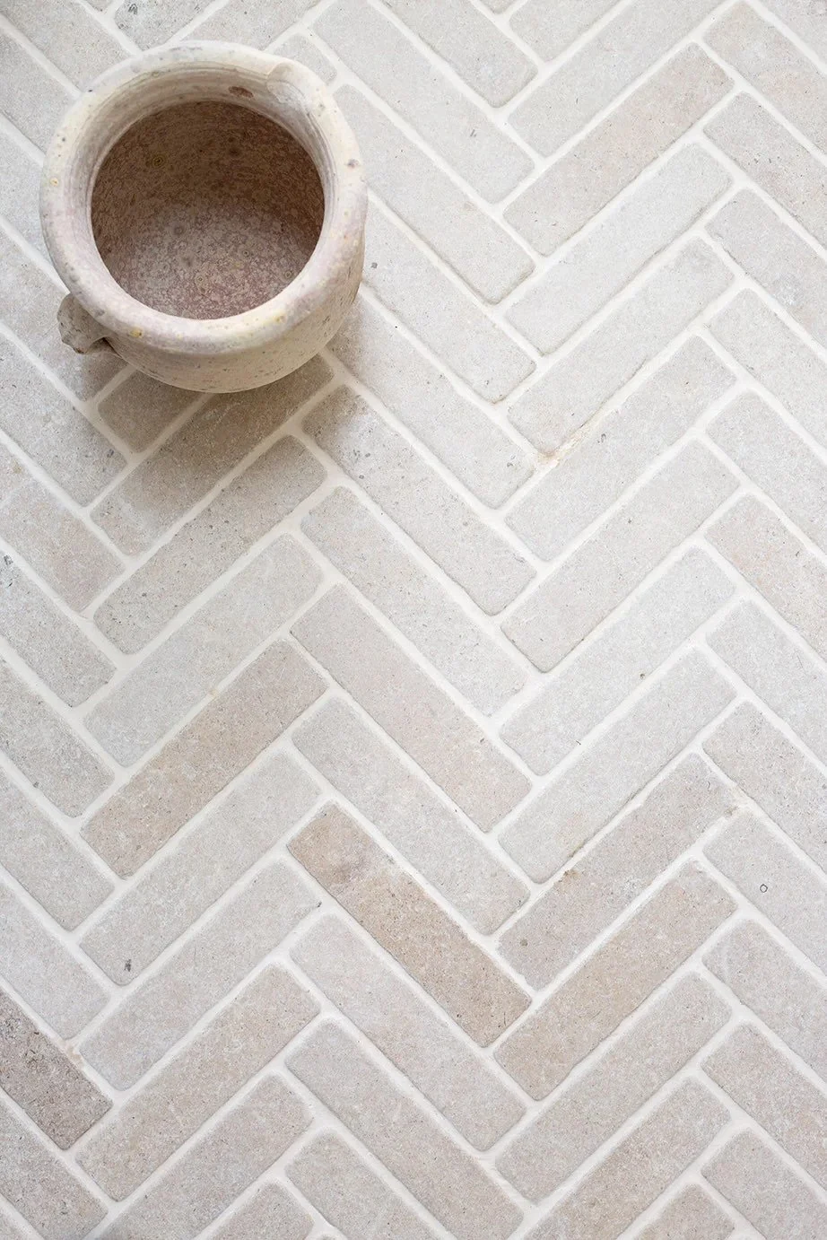 Top view of a beige ceramic flowerpot on a light-colored herringbone-patterned tiled floor.