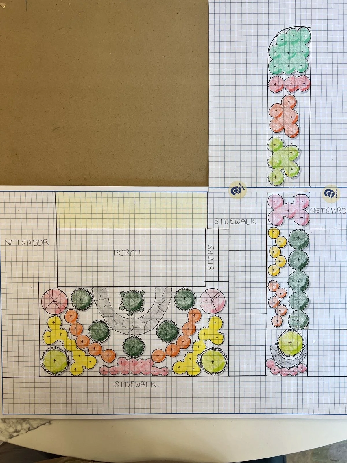 Hand-drawn landscape design plan on graph paper showing a backyard layout with a porch, side walk, trees, shrubs, and colored flower beds.