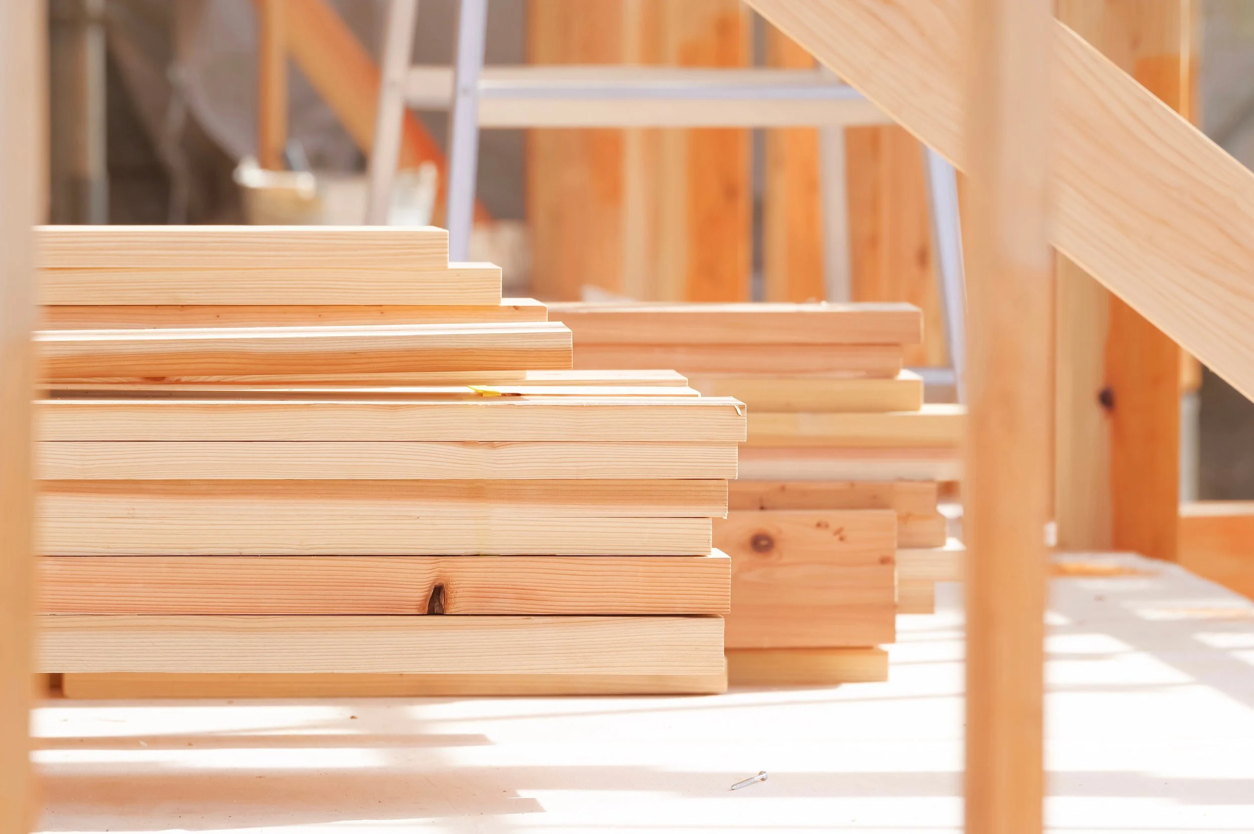 Stacks of light-colored wooden planks on a construction site for framing construction projects.
