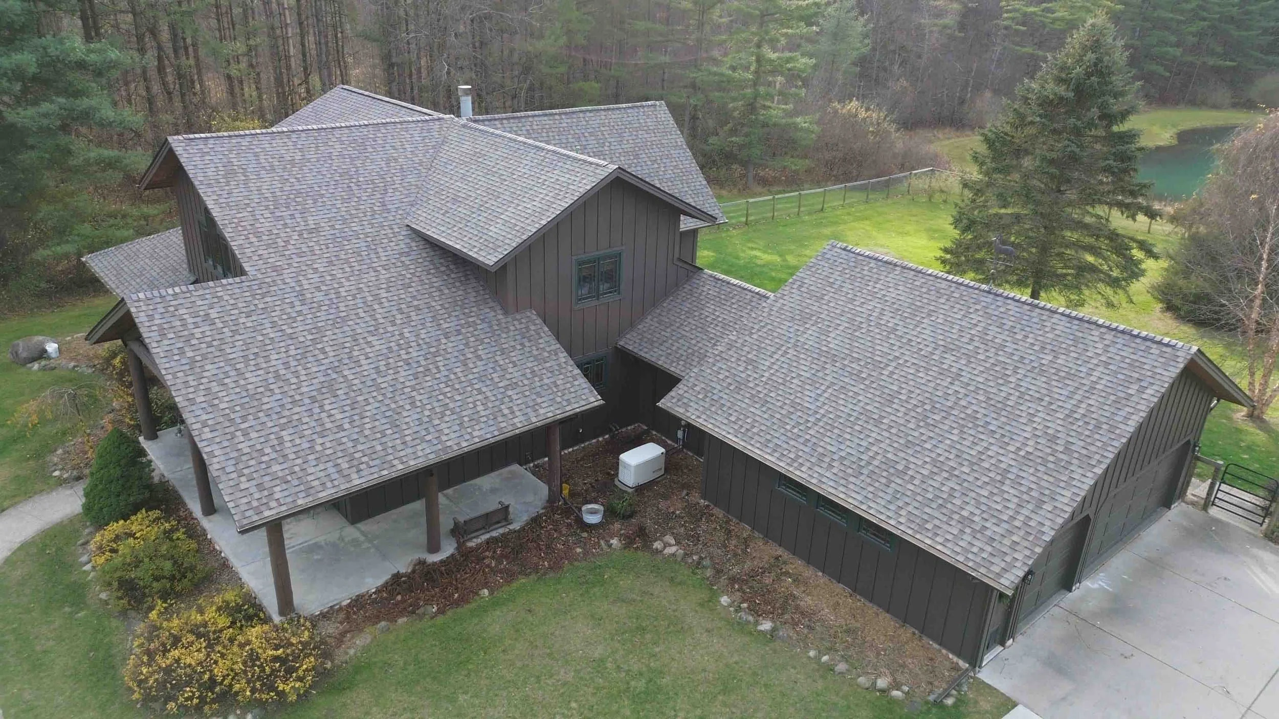 Aerial view of a house with brown shingle roof surrounded by grass and trees.
