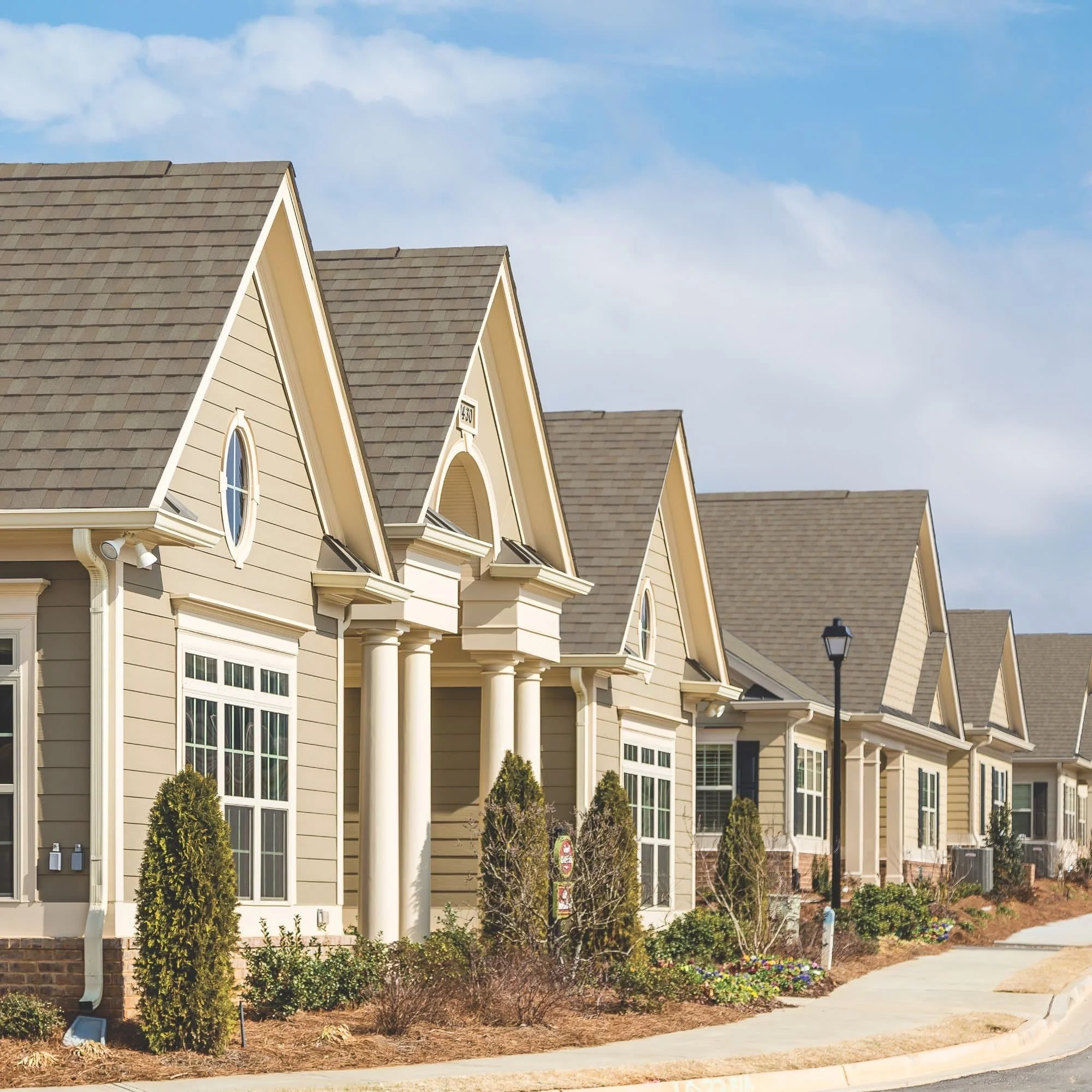 Row of suburban houses with gable roofs and landscaping under a clear blue sky.