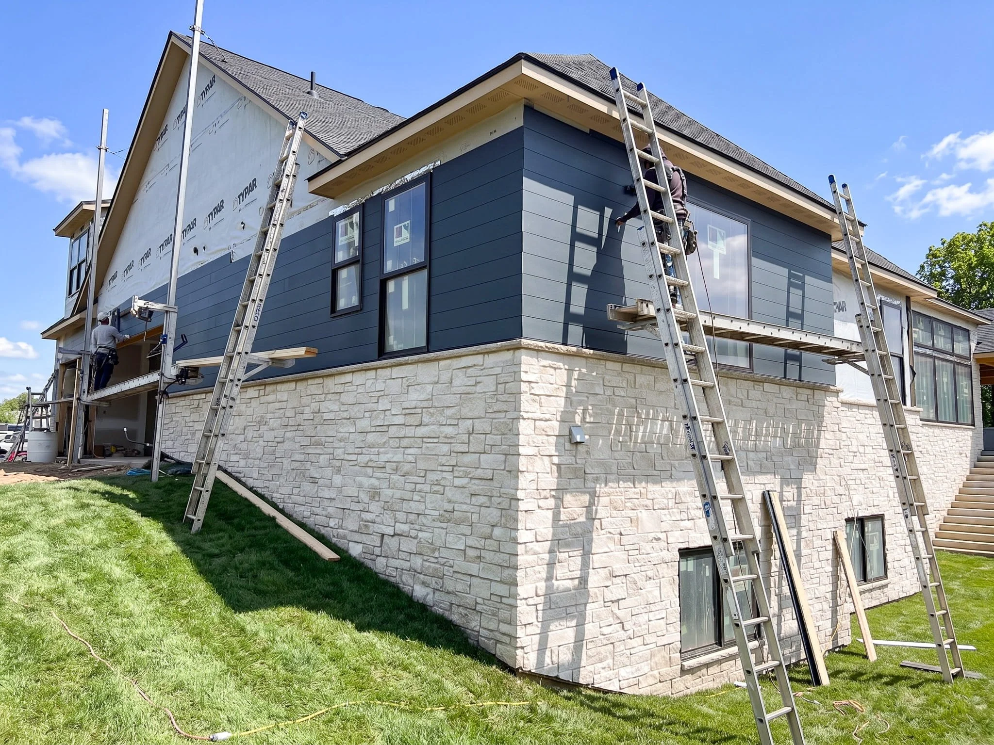 LP SmartSide engineered wood siding installation in progress on large two-story home with stone foundation and ladders on exterior