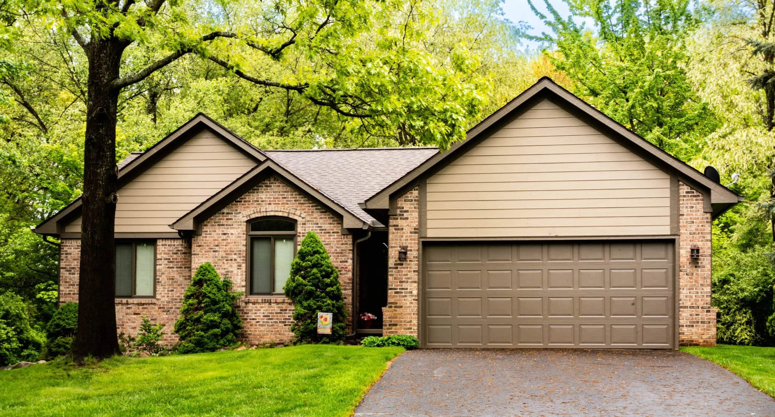 Single-story brick house with james hardie siding, two-car garage, large front windows, and trees and grass surrounding the home.