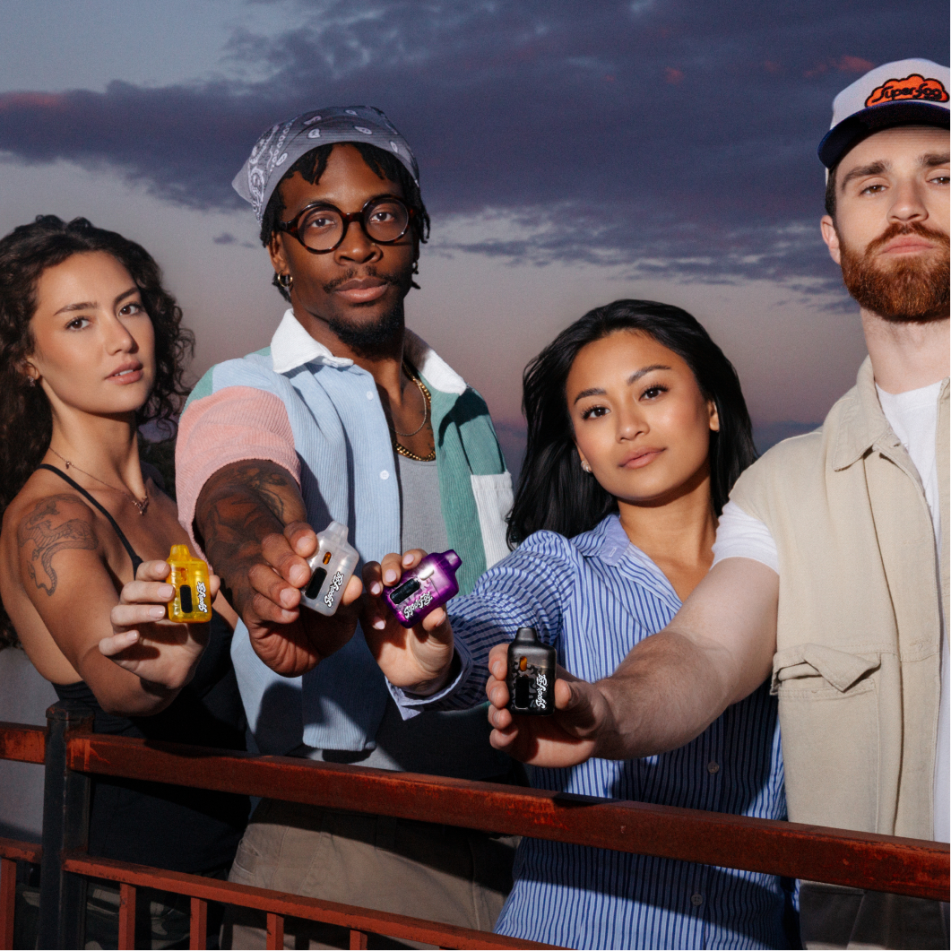 Group of five diverse young adults holding small electronic devices outdoors during sunset.