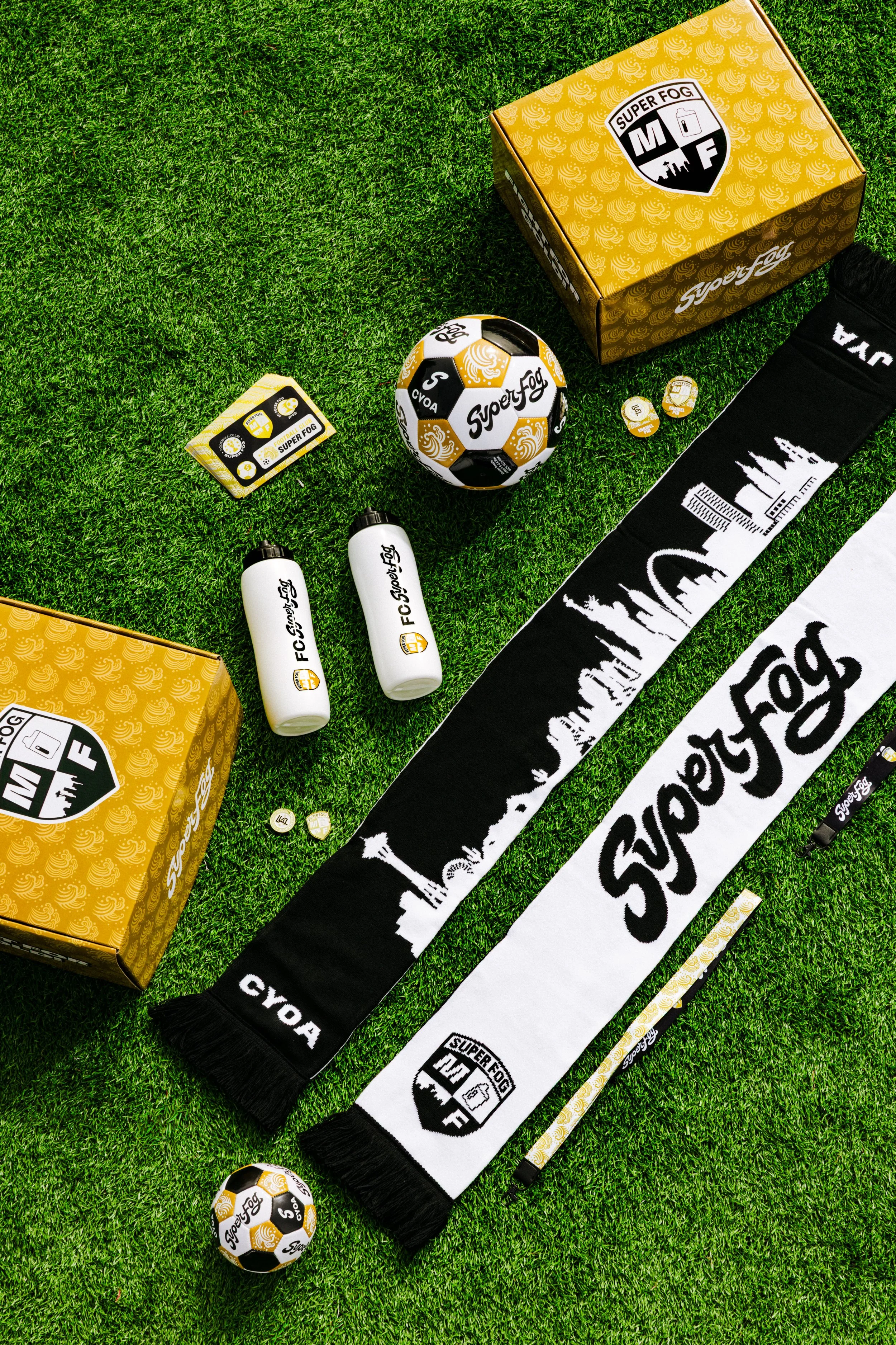 Soccer ball, two water bottles, a box, a scarf, a pencil, and small round tokens on green artificial grass.