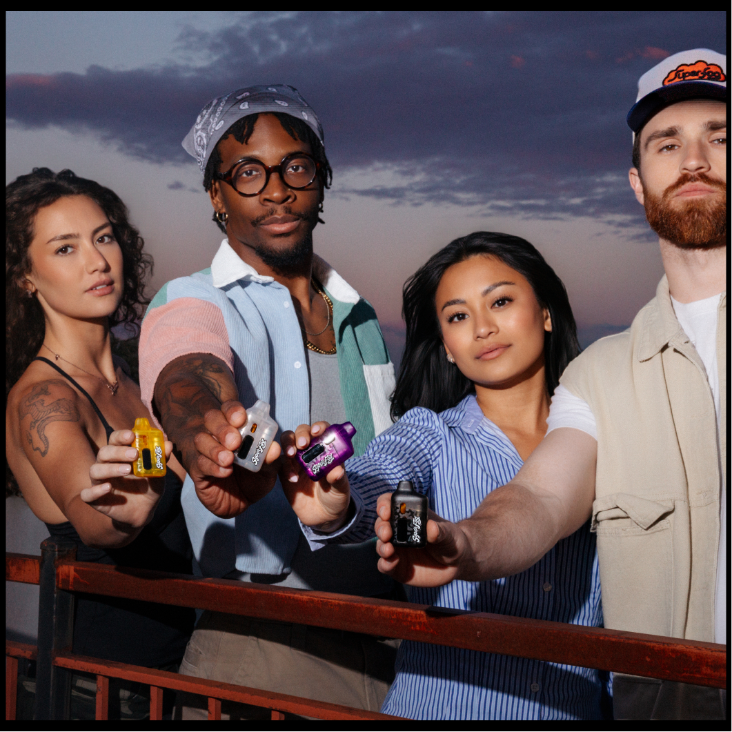 Group of five young adults standing outdoors during sunset, holding vape devices towards the camera.