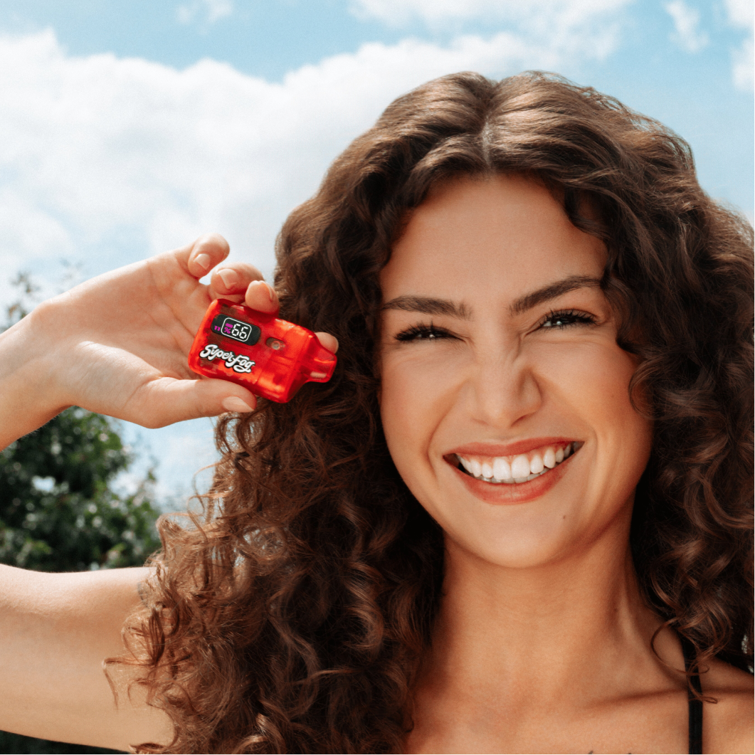 Smiling woman holding a small red device with a digital display outdoors.