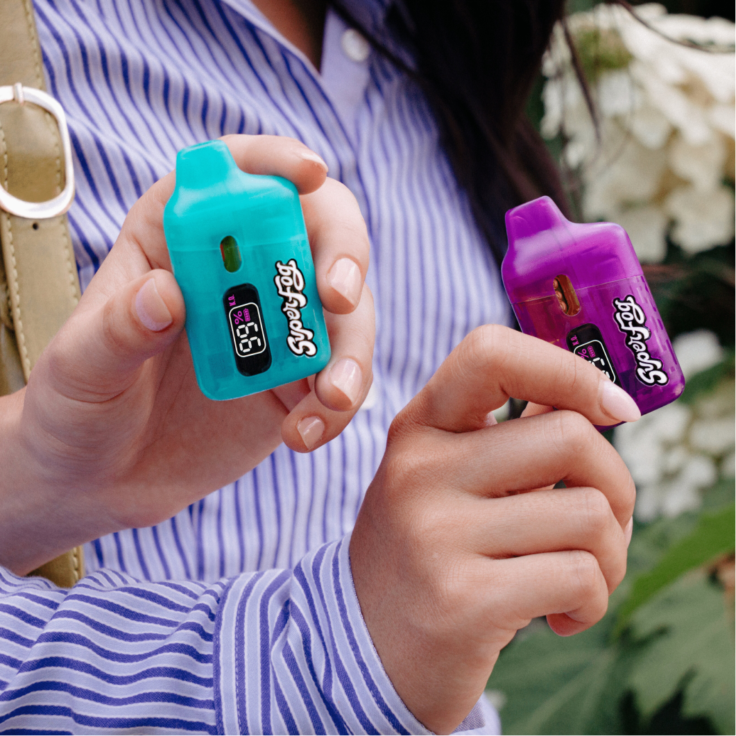 A person wearing a blue and white striped shirt holding a turquoise and a purple digital breathalyzer device, with a garden background.