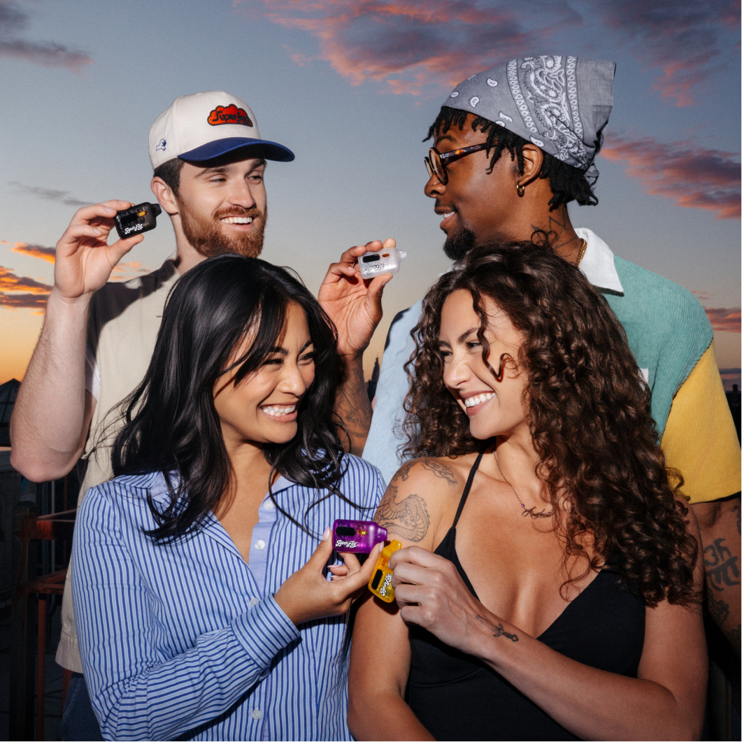 Four friends smiling and holding small cameras on a rooftop during sunset.