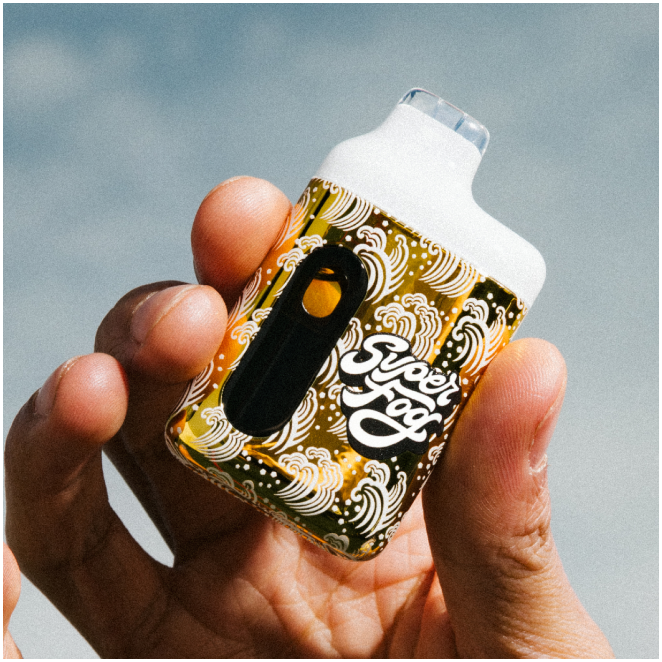 Close-up of a person holding a small object with intricate gold and black patterns, possibly a decorated spray bottle, against a light grey background.