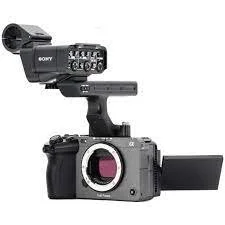 A small cinema camera with a lens is mounted on a shoulder rig with a top handle and external monitor.
