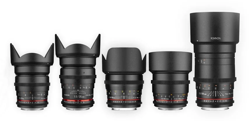 A collection of seven black cinema prime lenses of varying sizes are arranged in a row, each with distinct lens hoods.