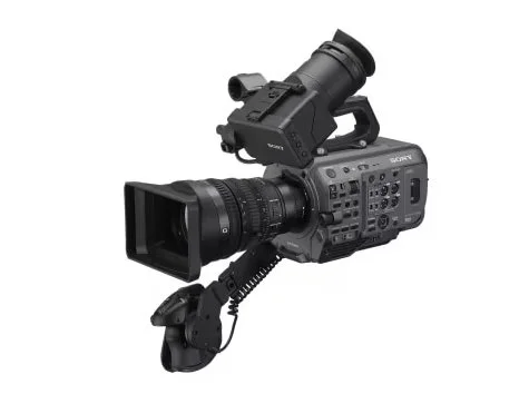 A professional video camera with a large lens is set up on a tripod with an attached microphone.