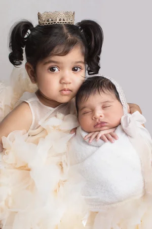 Toddler sister in a crown and cream tulle dress holding her newborn sibling in a bonnet, Mountain View newborn photographer