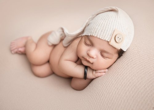 Newborn sleeping on her side in a cream knit cap on a soft beige backdrop, Mountain View newborn photography studio