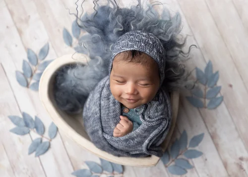 Newborn in a blue knit bonnet swaddled in a white heart-shaped bowl with blue leaves, Bay Area newborn photography session