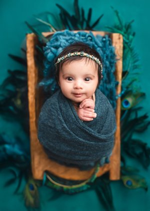 Wide-eyed newborn girl in a teal wrap in a wooden crate on a teal peacock feather backdrop, Mountain View newborn photographer